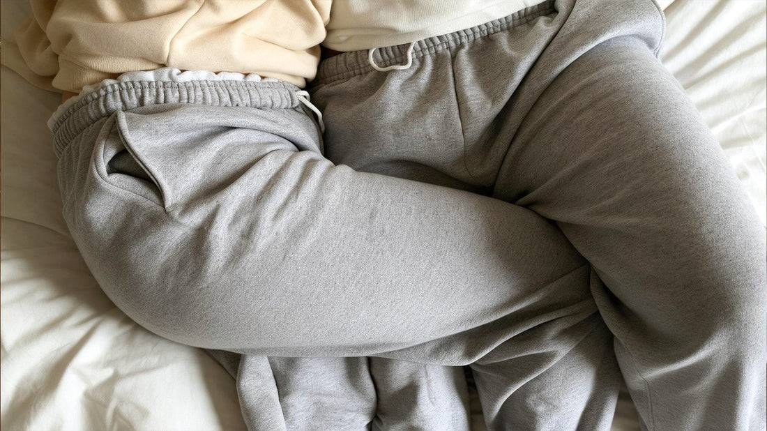 Close-up of two people in matching gray sweatpants cuddling together on a bed.