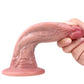 Don realistic dildo curved and held by hand, showing its flexible shaft and suction-cup base.